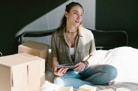Home Entrepreneurship - A Woman in Bed with Brown Boxes while Holding a Tablet