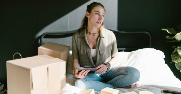 Home Entrepreneurship - A Woman in Bed with Brown Boxes while Holding a Tablet