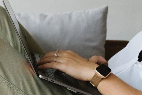 Home Business - Side view of crop unrecognizable female freelancer in casual clothes and smartwatch lying on comfortable sofa and working remotely on laptop