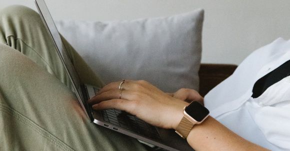 Home Business - Side view of crop unrecognizable female freelancer in casual clothes and smartwatch lying on comfortable sofa and working remotely on laptop